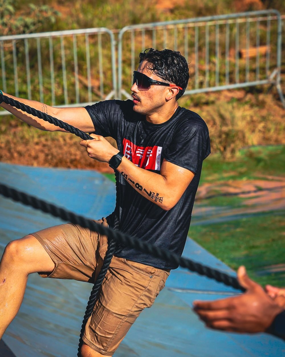 Gustavo Rodrigues subindo em uma corda durante uma prova de obstáculos, com camiseta da BJJ House